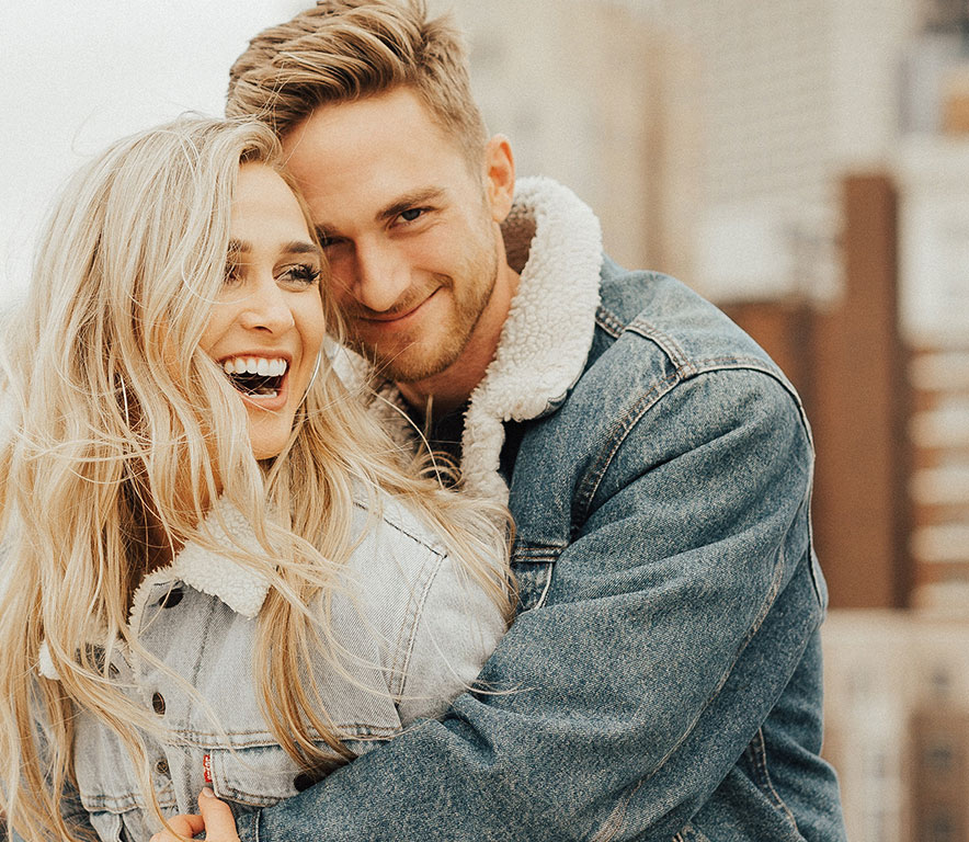 man hugs women from behind both are smiling