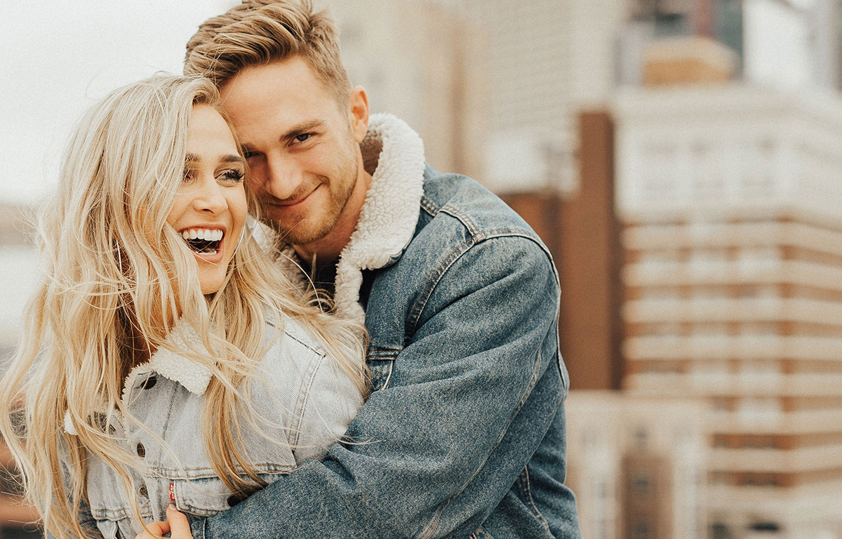 man hugs women from behind both are smiling