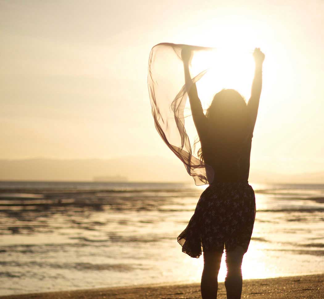 women with hands raised on beach in sunshine