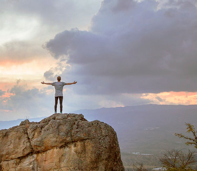 man reaches top of mountain and outstretches arms