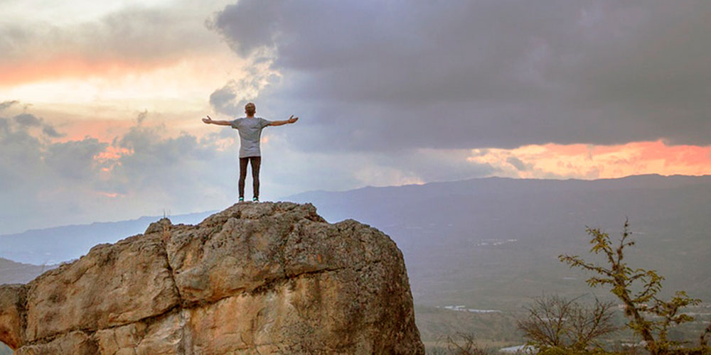 man reaches top of mountain and outstretches arms